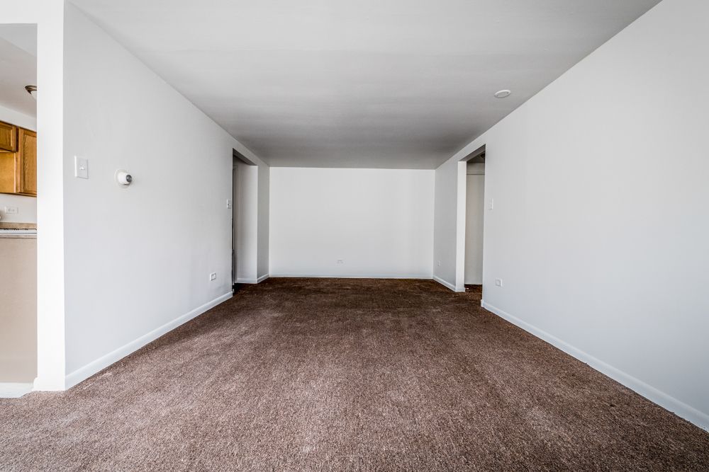 Empty living room with brown carpet, white walls, and doorways.