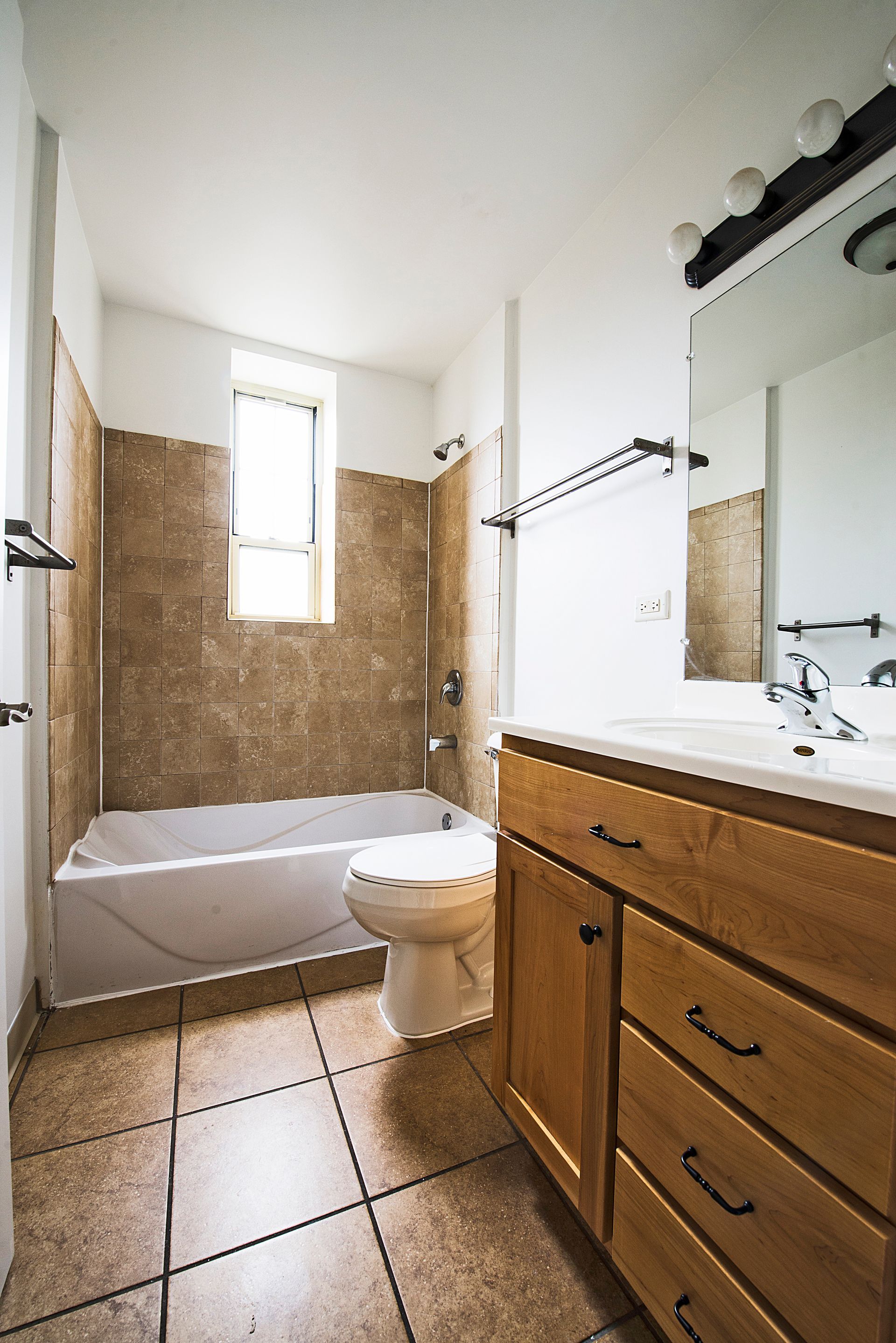 Bathroom with tile walls and floor, tub, toilet, and wooden vanity.