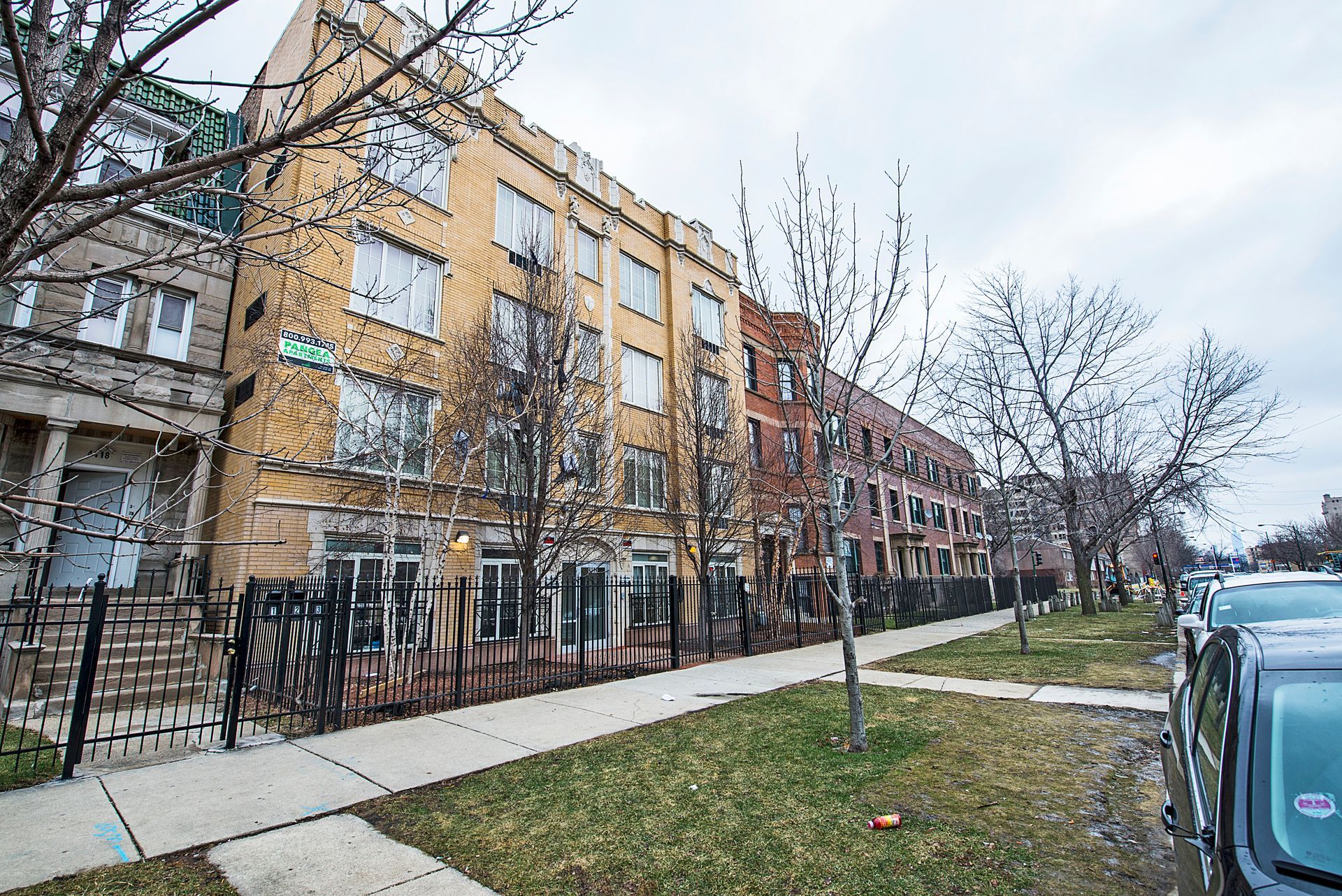 Apartment buildings on a city street, with cars parked, overcast sky.