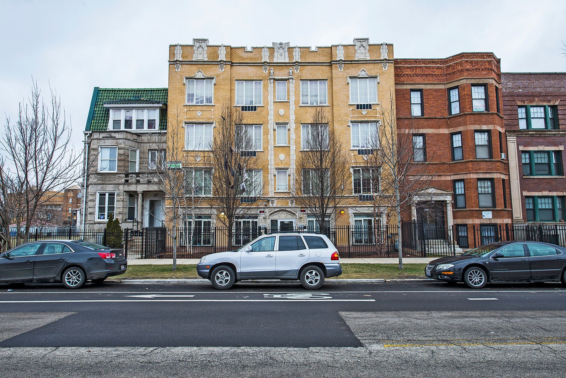 Row of apartment buildings with parked cars on a city street.