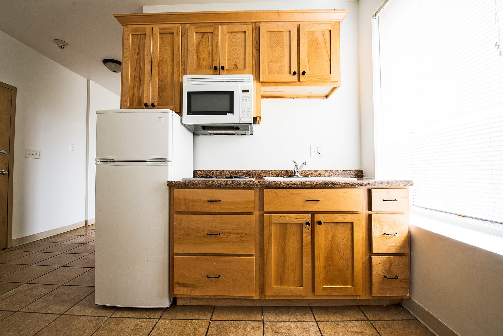 Small kitchen with wooden cabinets, microwave, sink, and refrigerator.