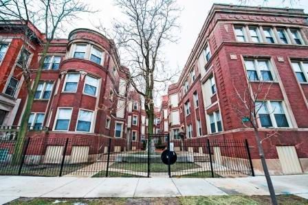 Brick apartment buildings with a small courtyard behind a black fence.