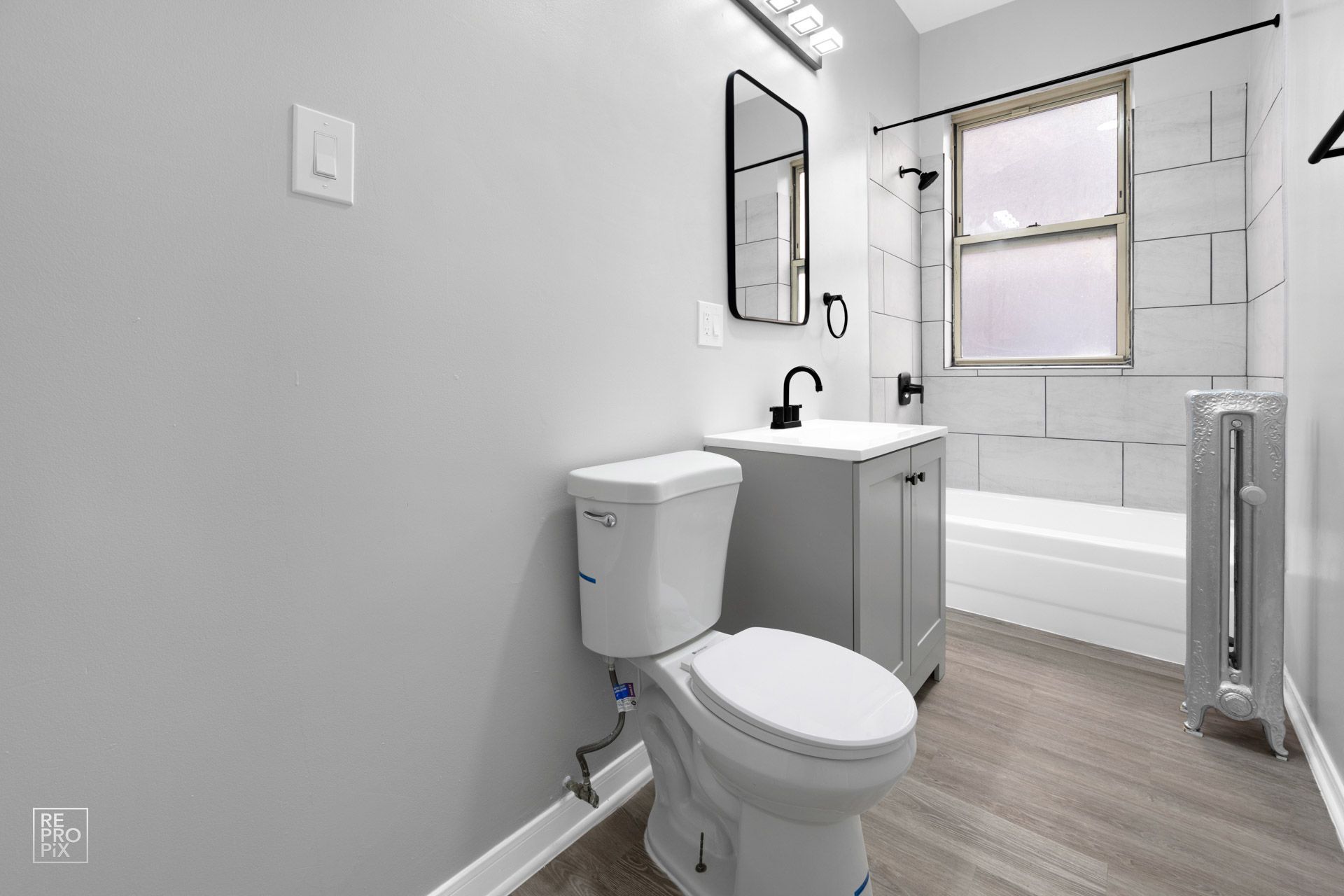 Bathroom with gray walls, toilet, vanity, and window with white subway tile.