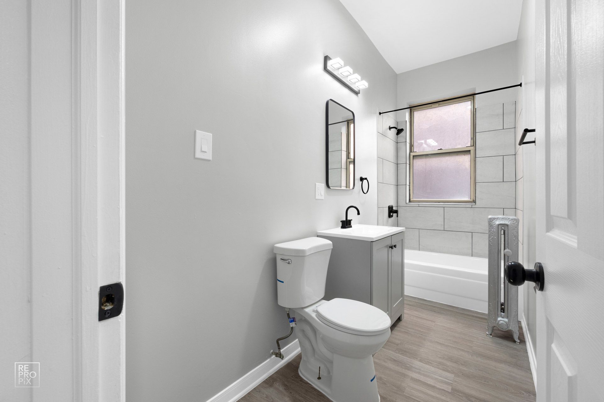 Bathroom with gray walls, white fixtures, wood-look floor, and black accents.