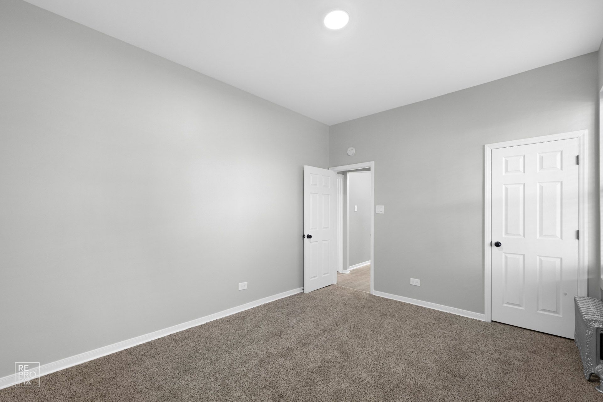 Empty room with gray walls, white doors, and brown carpet.