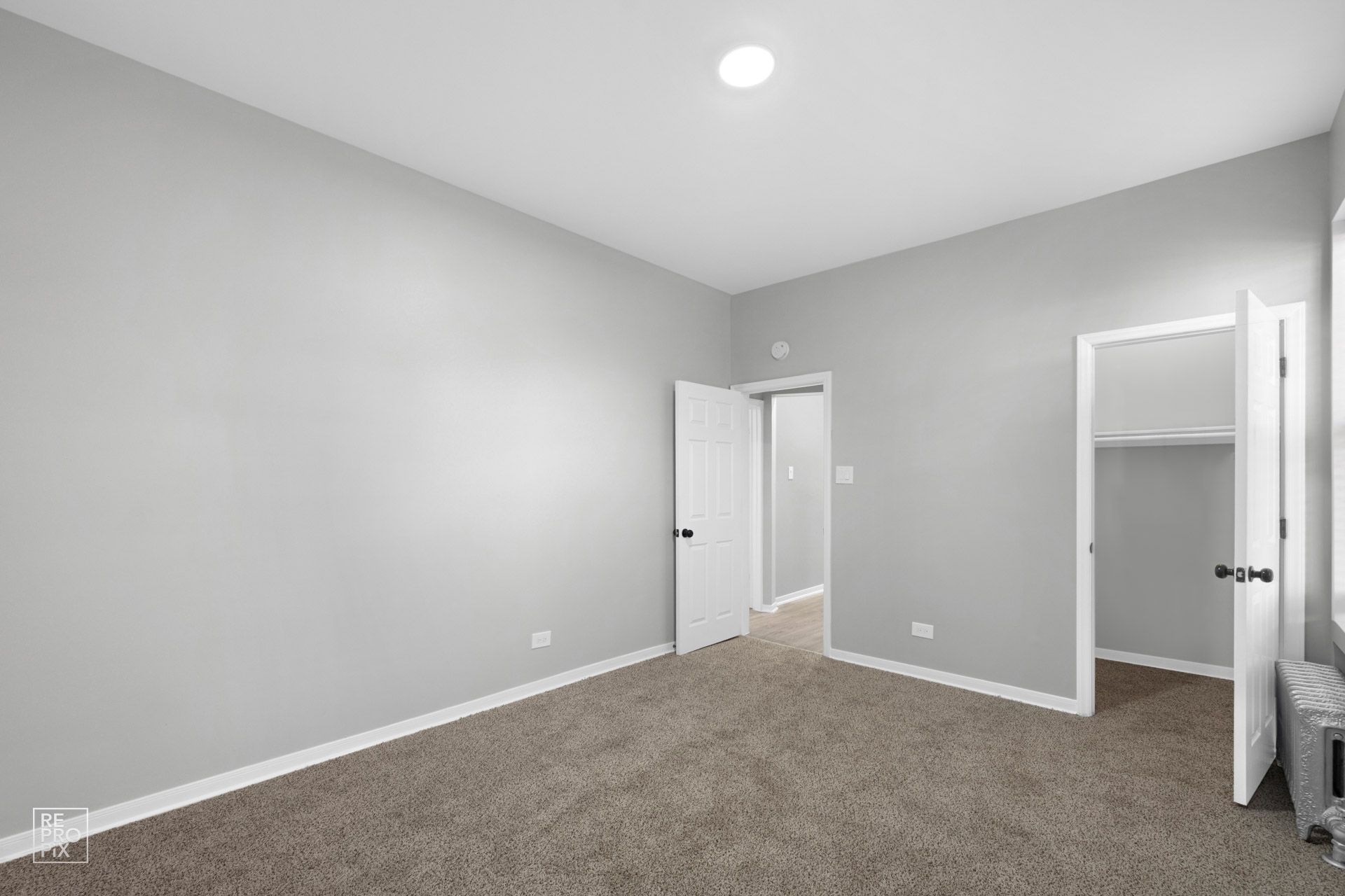 Empty room with grey walls, brown carpet, and open doors.