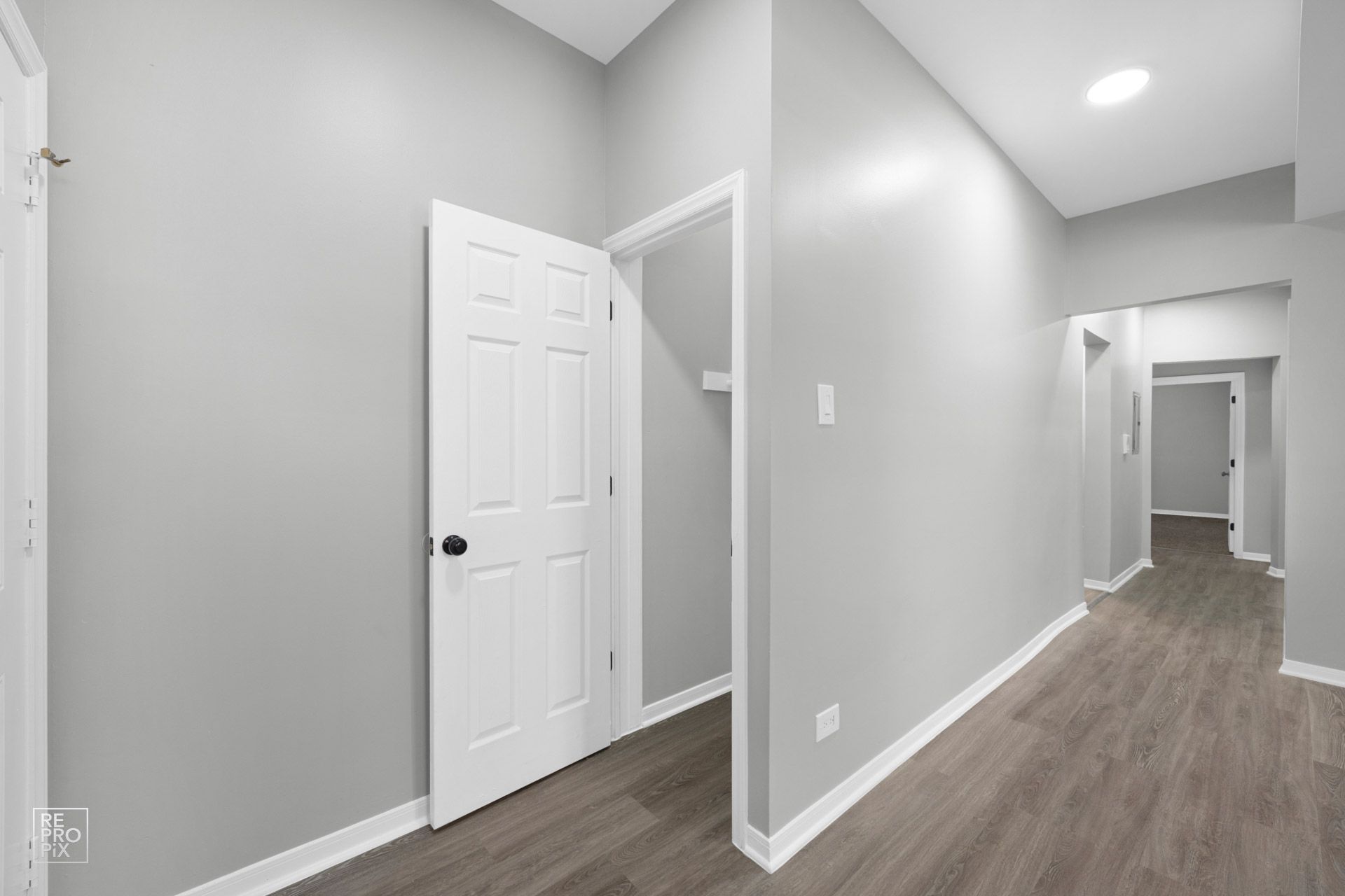 Hallway with gray walls, white door and trim, leading to other rooms.