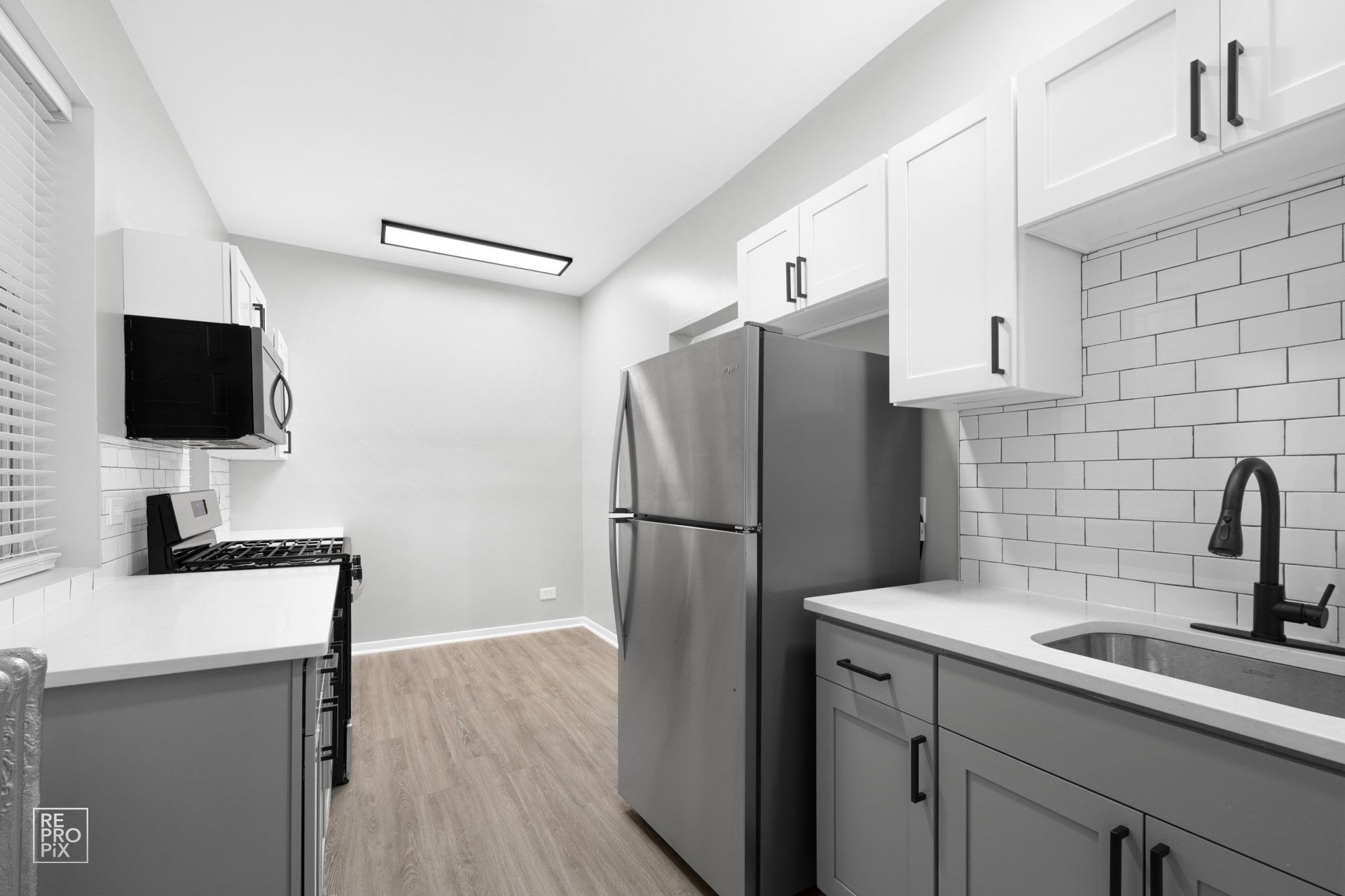 Modern kitchen with white cabinets, stainless steel fridge, and gray countertops.