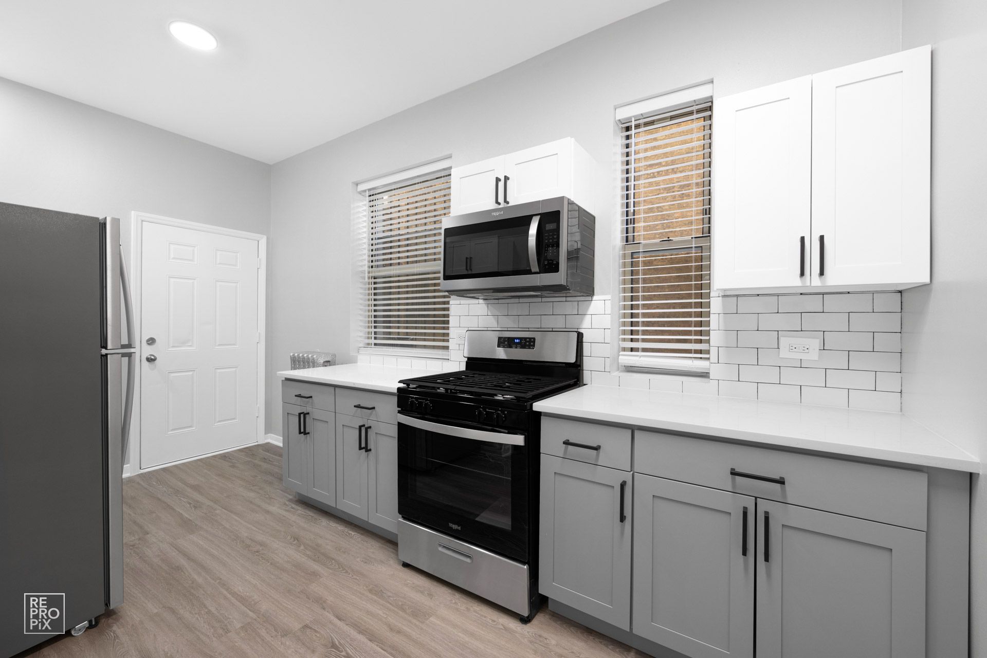 Modern kitchen with gray and white cabinets, stainless steel appliances, and wood floors.