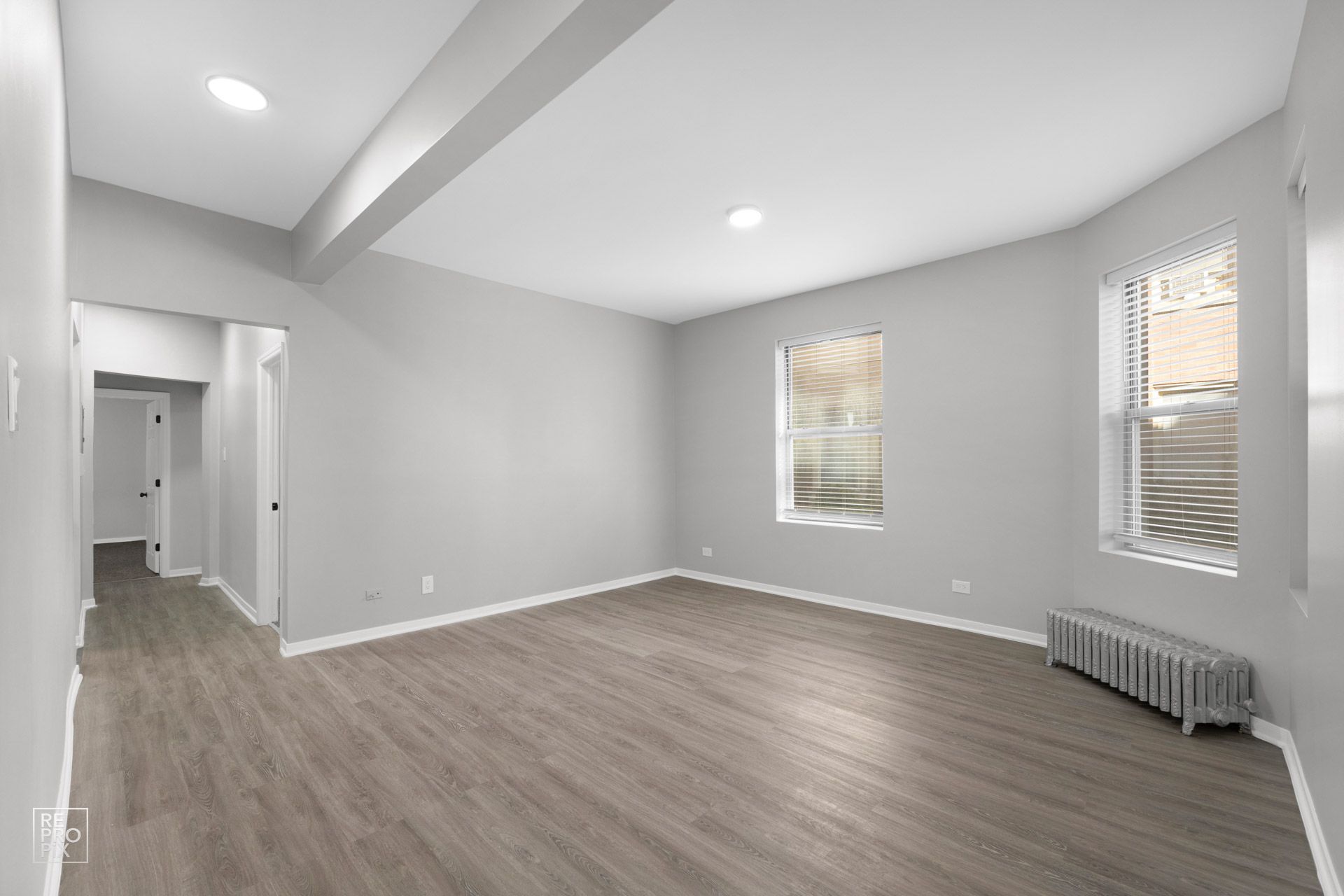 Empty living room with gray walls, wood-look flooring, and windows.