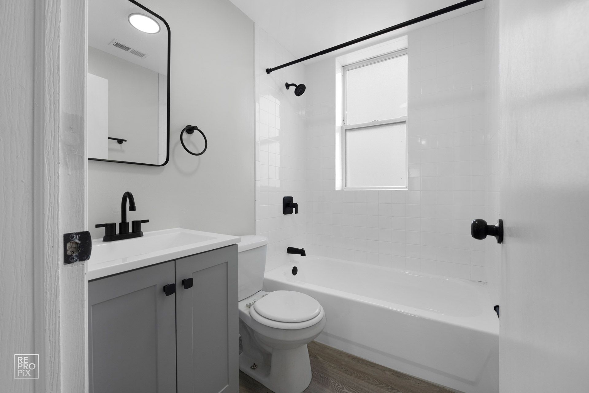 Gray and white bathroom with a toilet, vanity, and bathtub. Black fixtures.