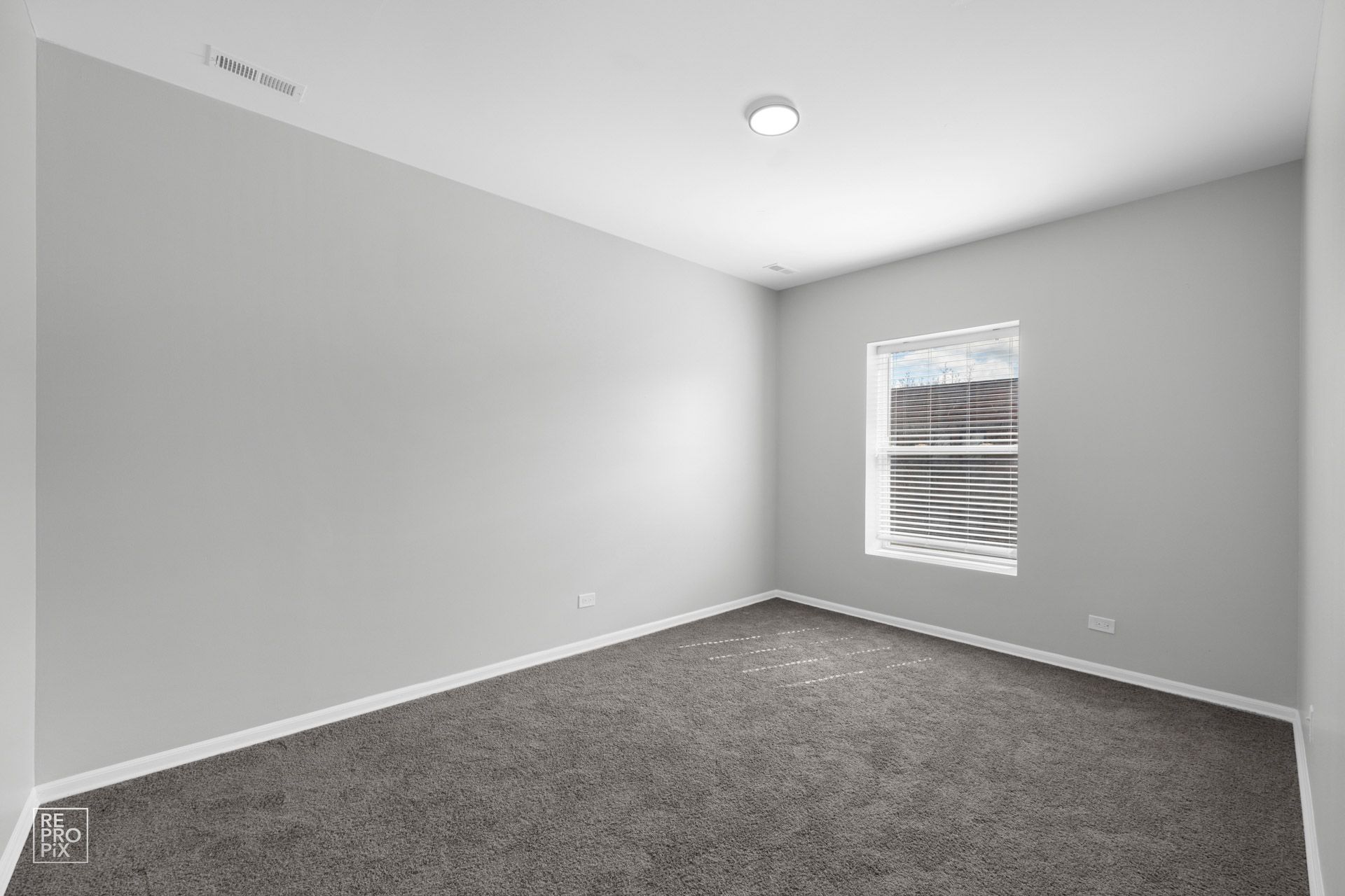 Empty room with gray walls and carpet, small window, and ceiling light.