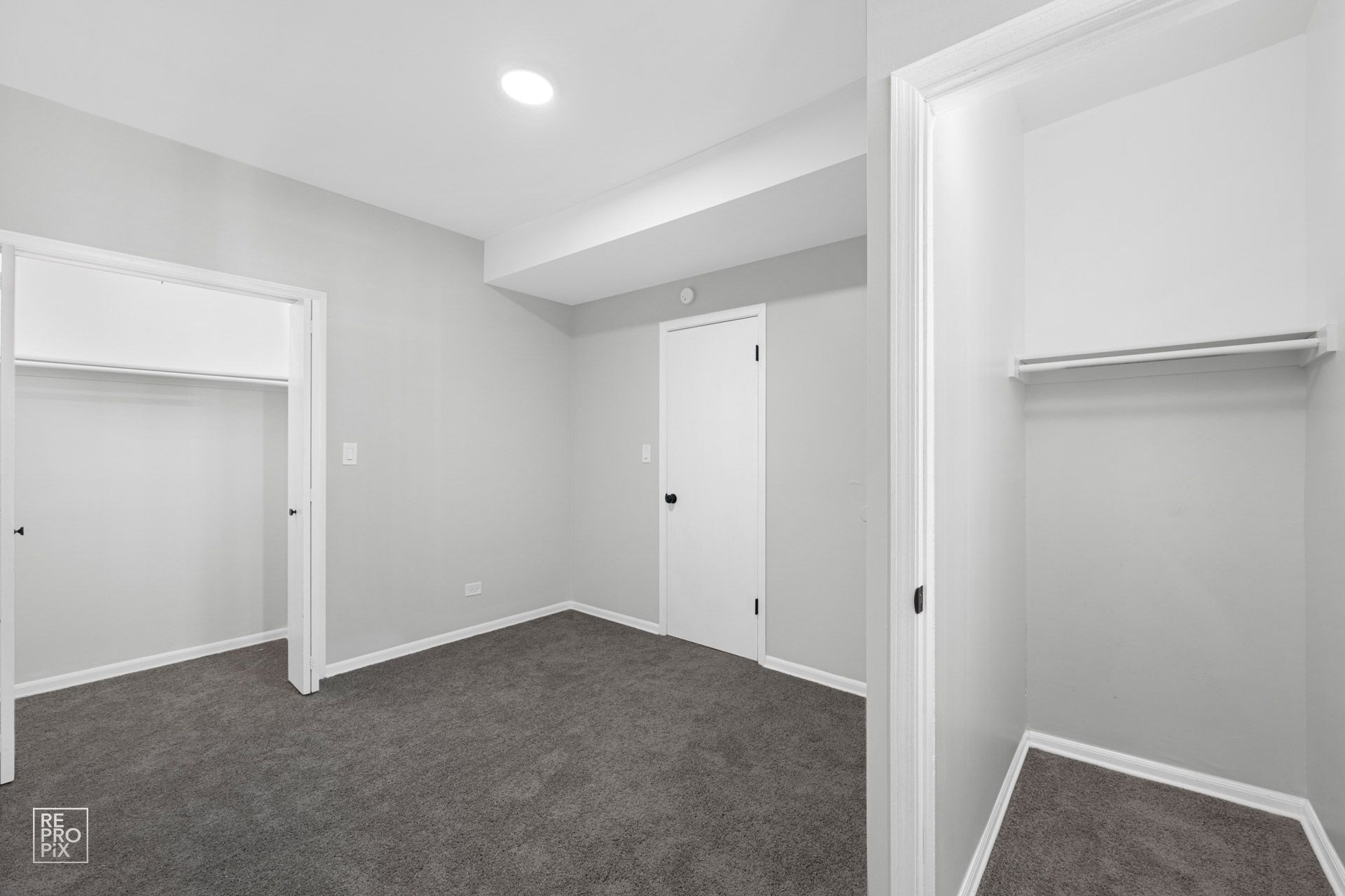 Empty bedroom with gray carpet, two closets, and a closed door.