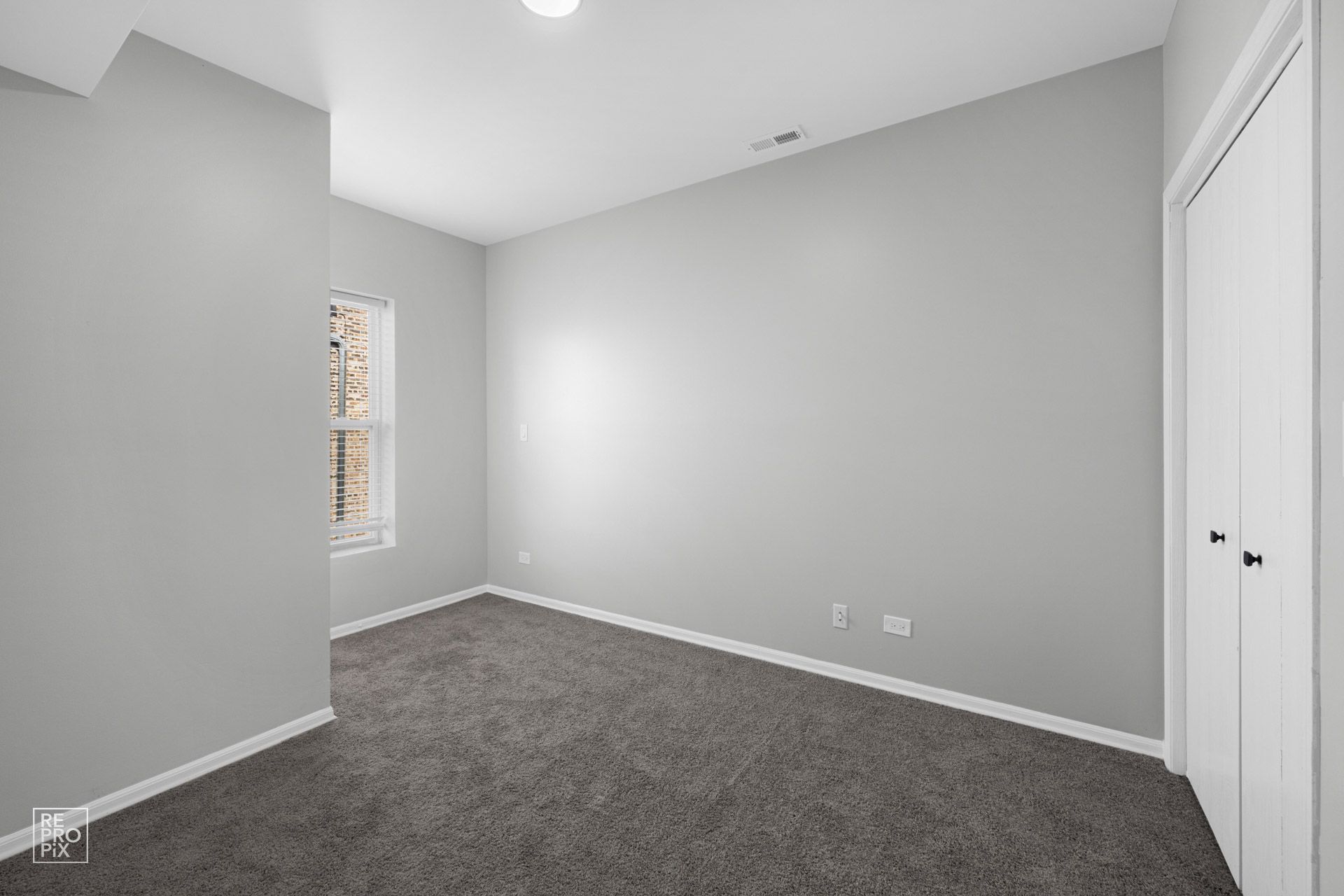 Empty room with gray carpet, walls, and a white closet. A window is on the left.