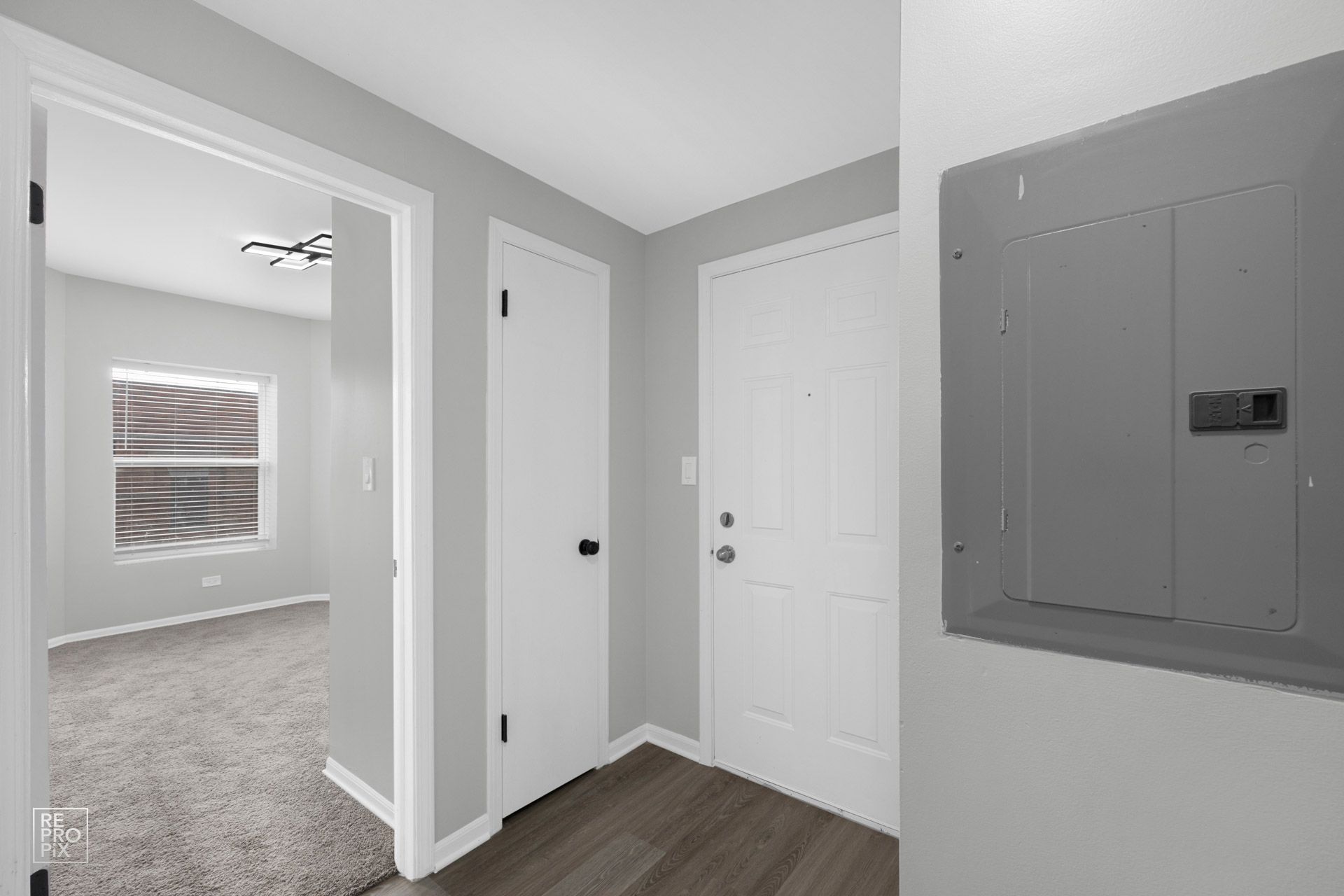 Interior hallway with gray walls, white doors, and a circuit breaker box. Doorway to a carpeted room.