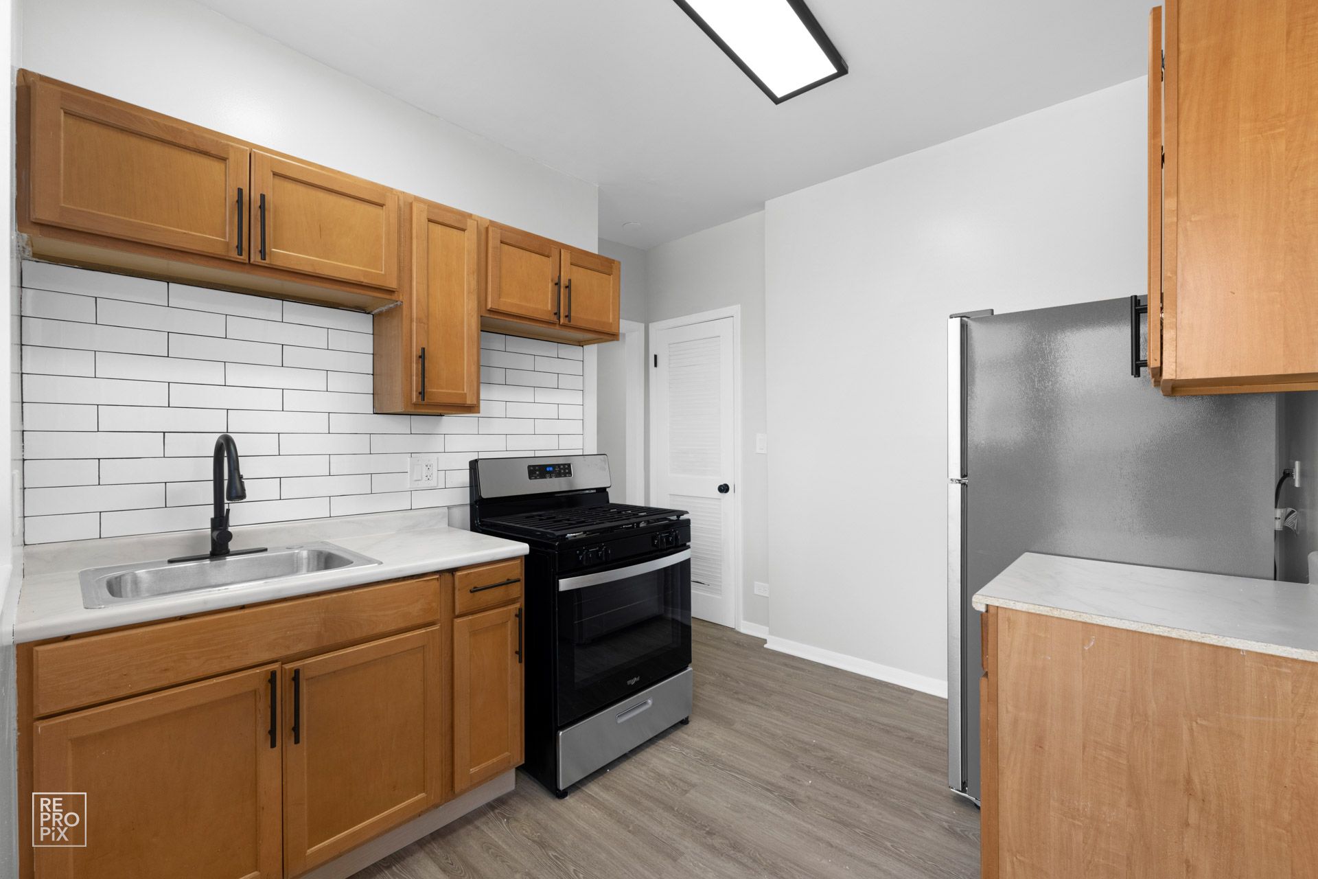 Kitchen with light wood cabinets, white countertops, stainless steel appliances, and a white brick-style backsplash.