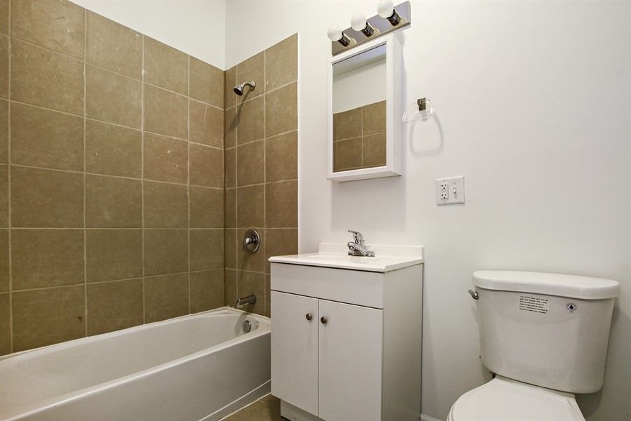 Bathroom with bathtub, sink, toilet, and tan tile shower wall. White and beige tones.
