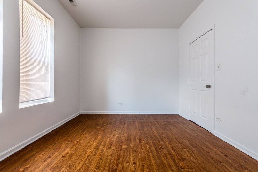 Empty room with wood-look floor, white walls, a window with blinds, and a closed door.