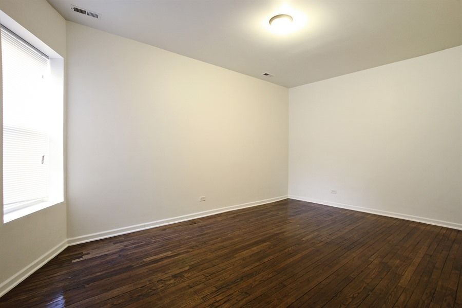 Empty room with dark hardwood floors, white walls, and a window on the left.