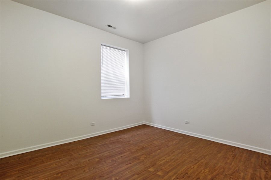 Empty room with wood-look floor, white walls, small window with blinds, and ceiling light.