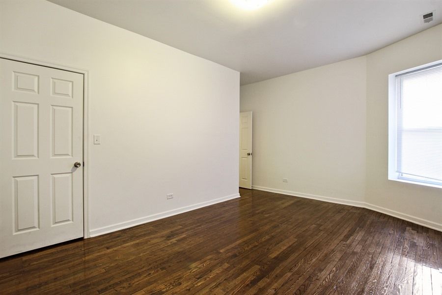 Empty room with hardwood floors, white walls, two white doors, and a window with blinds.