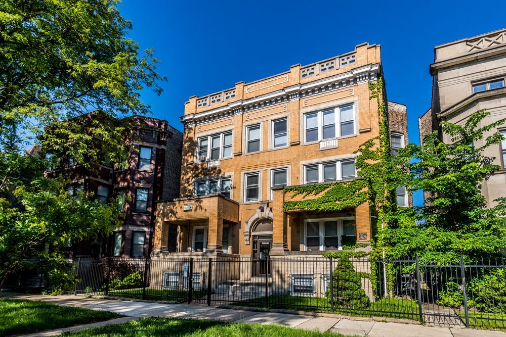 Multi-story brick apartment building with wrought iron fence on a sunny day.