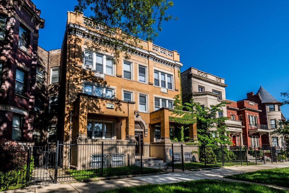 Row of Chicago brick buildings on a sunny day. Light orange and red facades, wrought-iron fences, green trees.