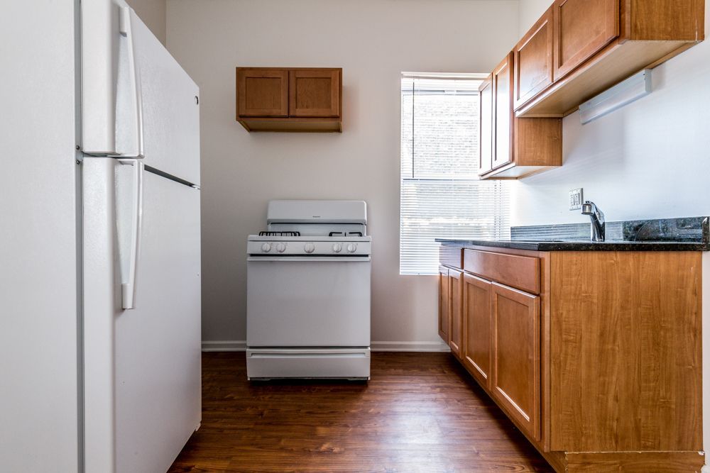 Small kitchen with white appliances, wooden cabinets and flooring, and a window.