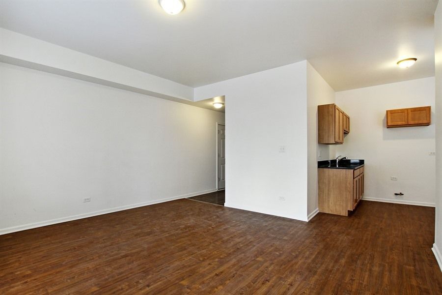 Empty apartment interior with wooden floors, white walls, and a small kitchen area.