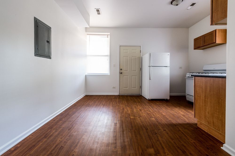 Empty kitchen with wood-look floor, white walls, and appliances. Includes cabinets, fridge, stove, and an electrical panel.