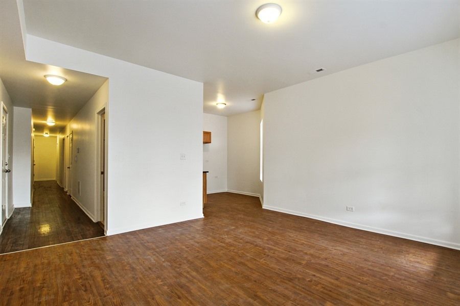 Empty apartment interior with wood flooring, white walls, and hallway.