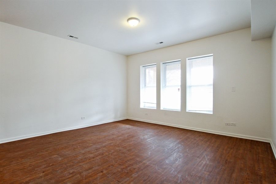Empty room with hardwood floors, white walls, and three windows.
