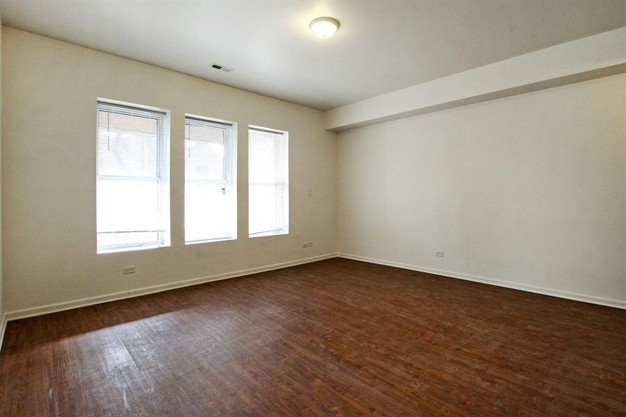 Empty room with three windows, wood floor, and beige walls.