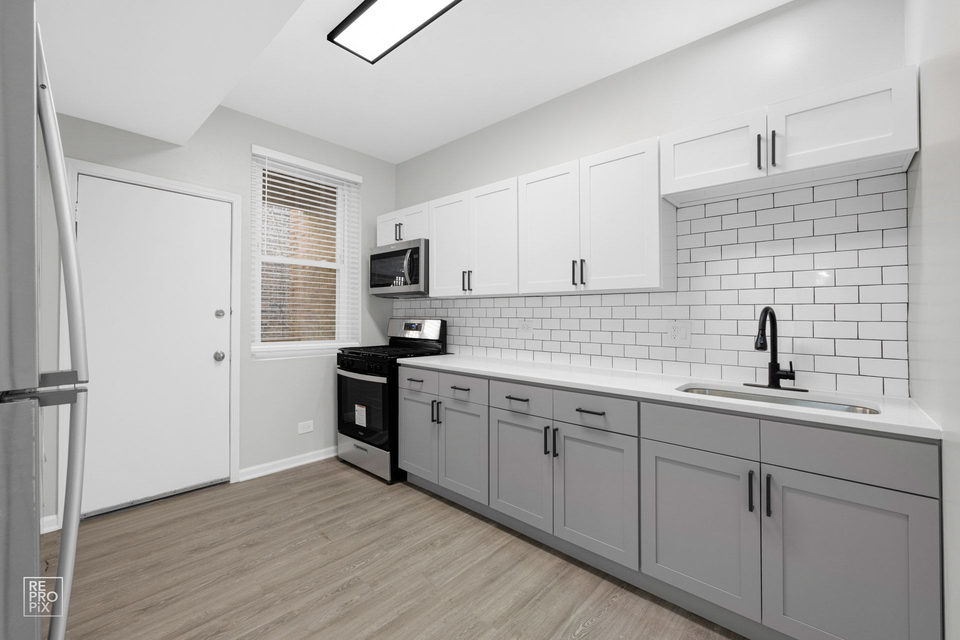 Gray and white kitchen with cabinets, stove, microwave, and sink.