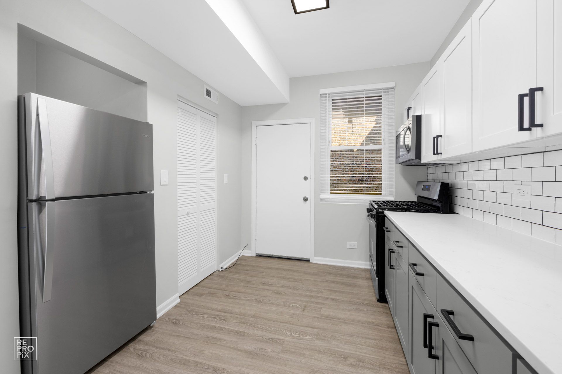 Kitchen with stainless steel fridge, white countertops, gray cabinets, and a white door.