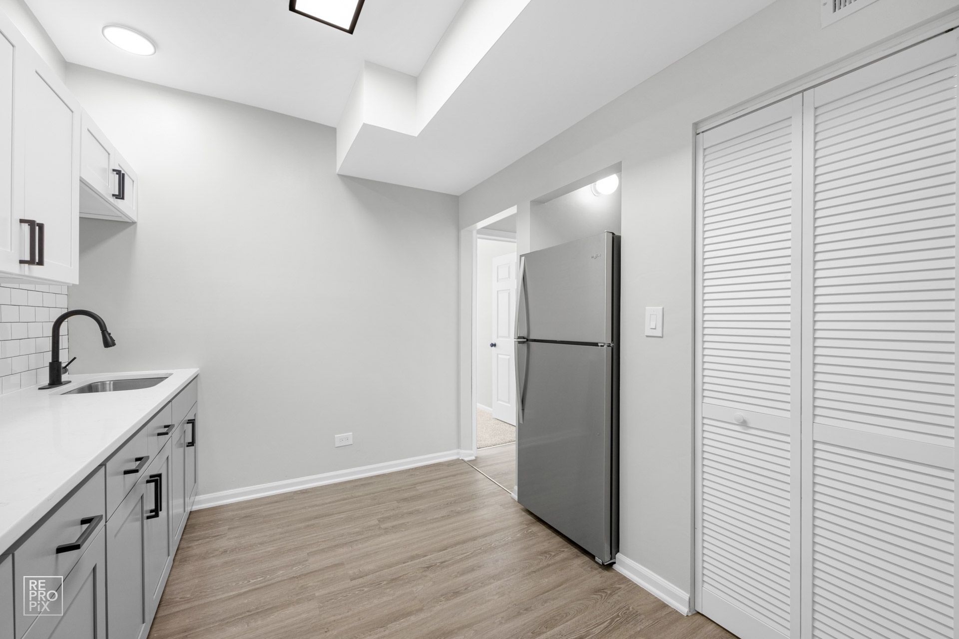 Kitchen with gray cabinets, white countertops, stainless fridge, and white louvered closet doors.