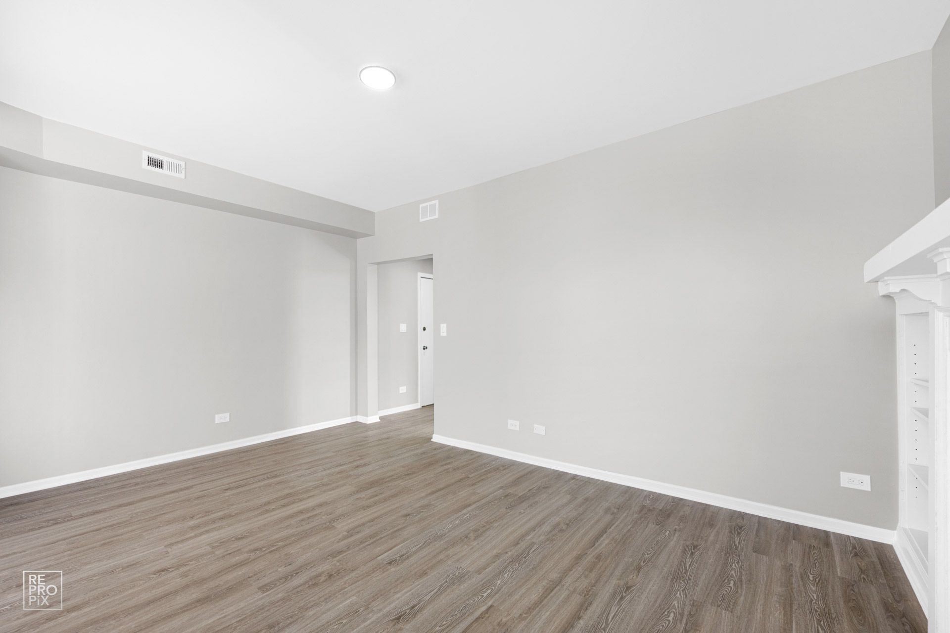 Empty room with gray walls and wood-look flooring. A doorway leads to another room.