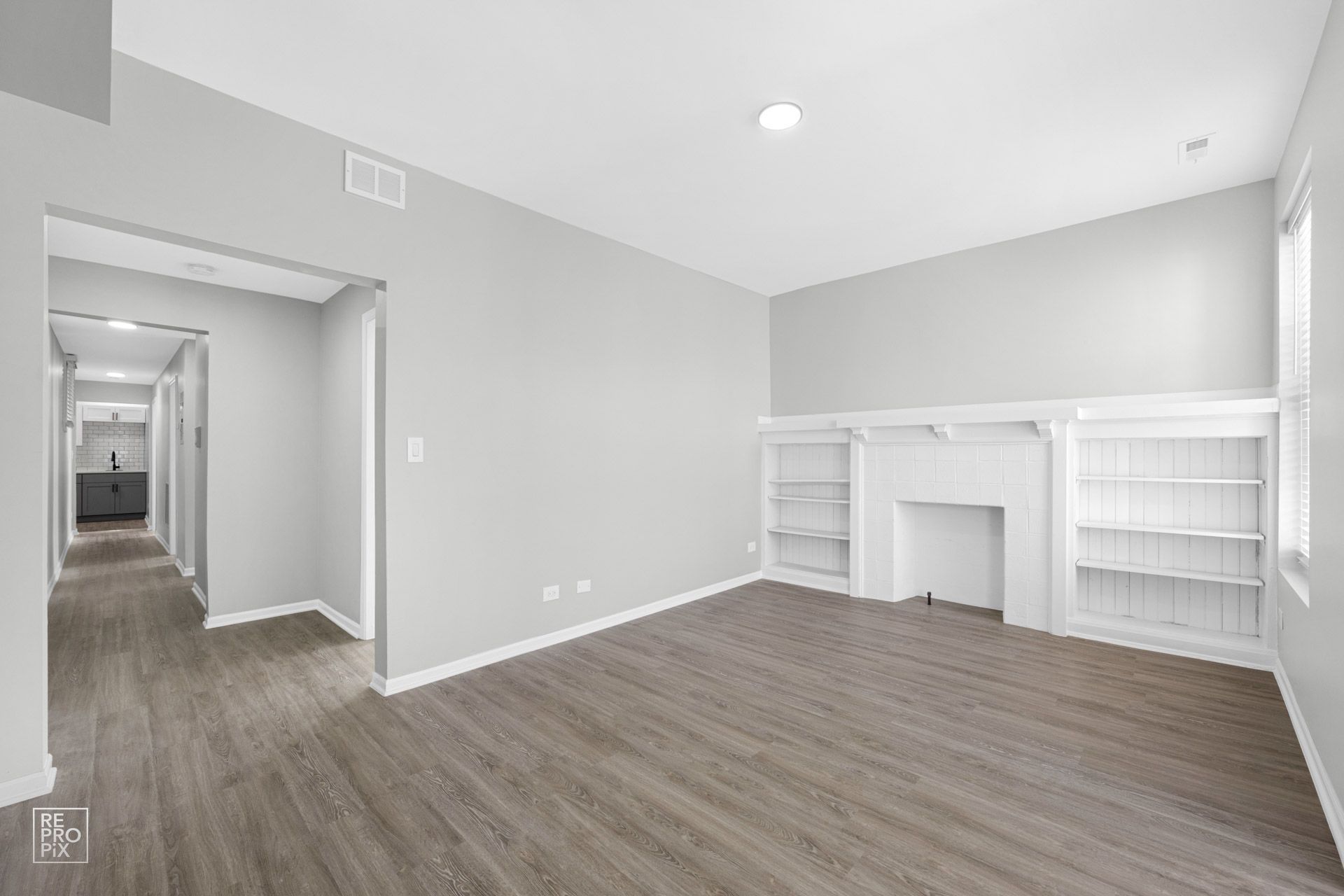 Empty living room with gray walls, hardwood floor, fireplace, and built-in shelves.