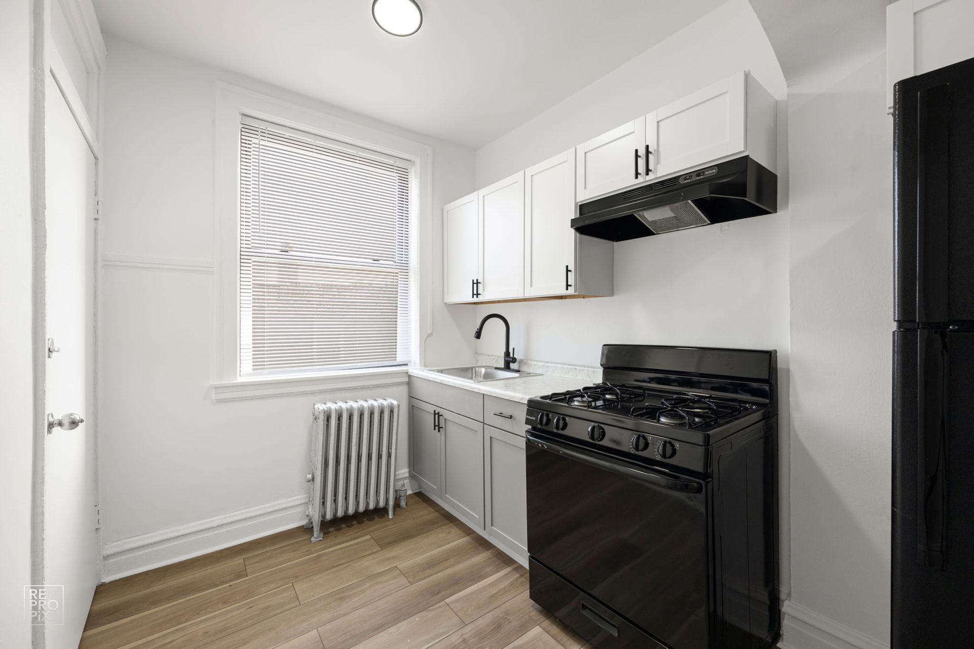 Small kitchen with white cabinets, black appliances, window, and wood-look flooring.