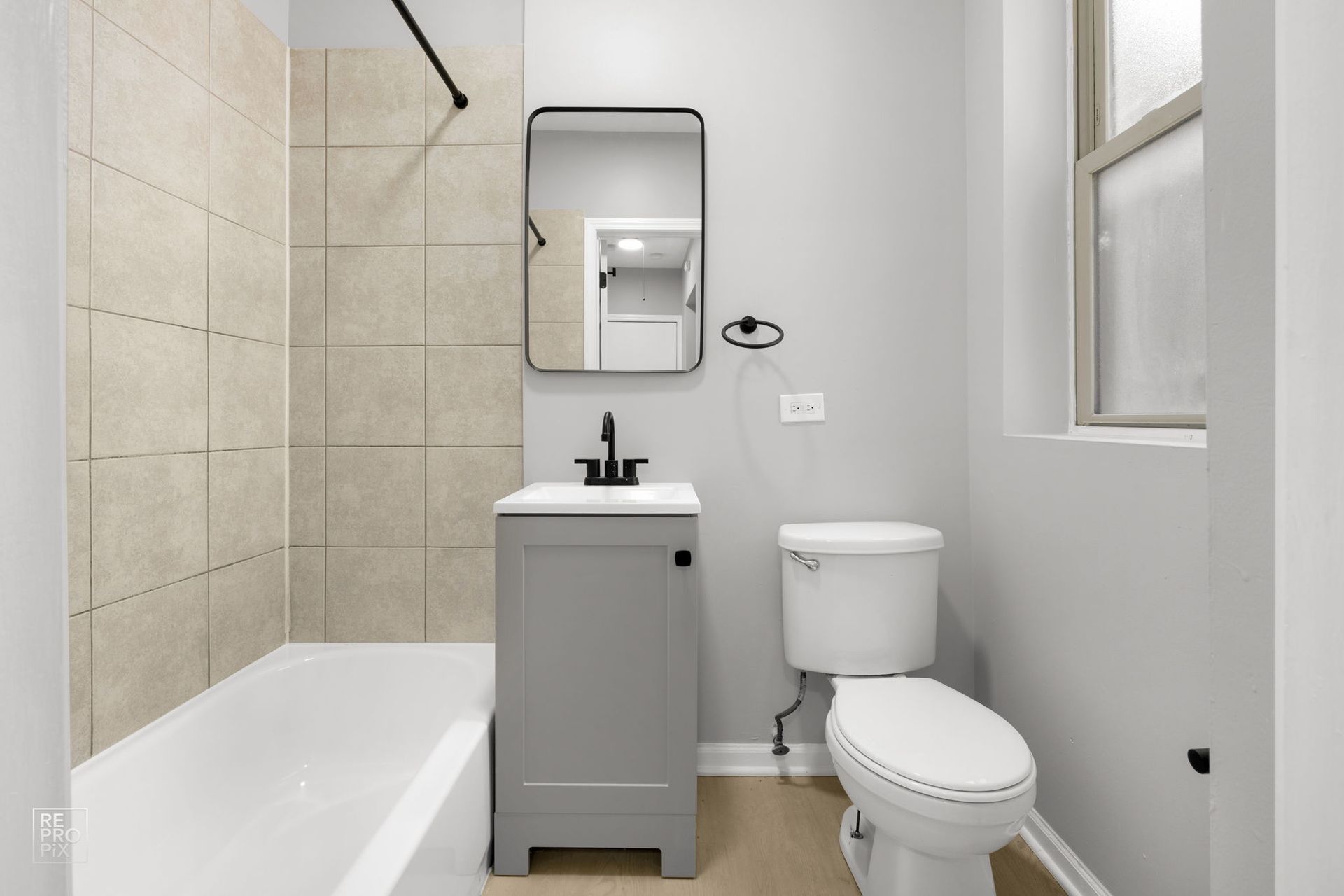 Bathroom with a gray vanity, toilet, mirror, and beige tiled shower area.