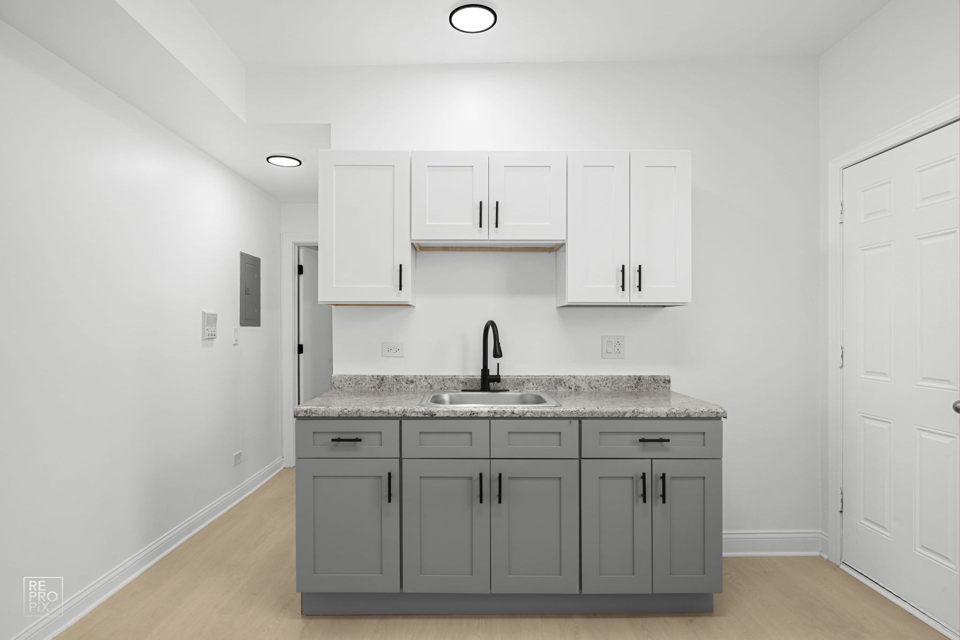 Small kitchen with gray and white cabinets, black faucet, and light-colored flooring.
