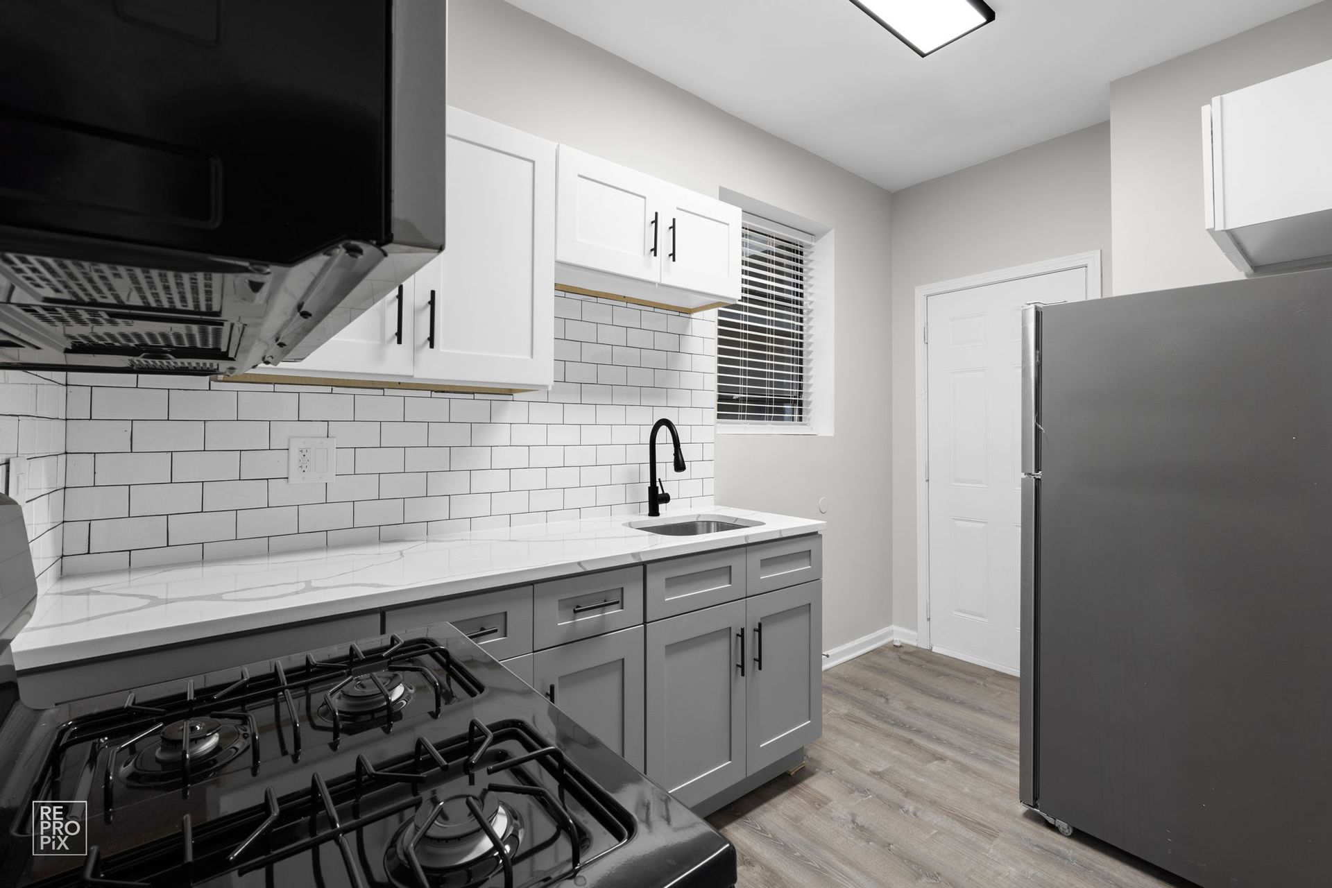 A modern kitchen featuring gray and white cabinets, black appliances, and white subway tile backsplash.
