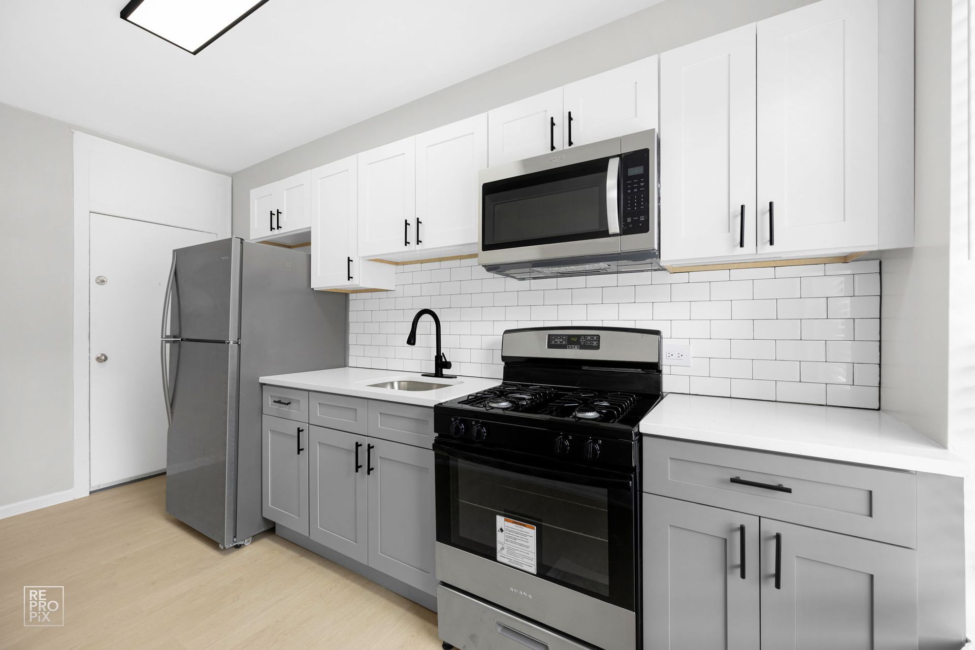 Kitchen with white and gray cabinets, stainless steel appliances, and subway tile backsplash.
