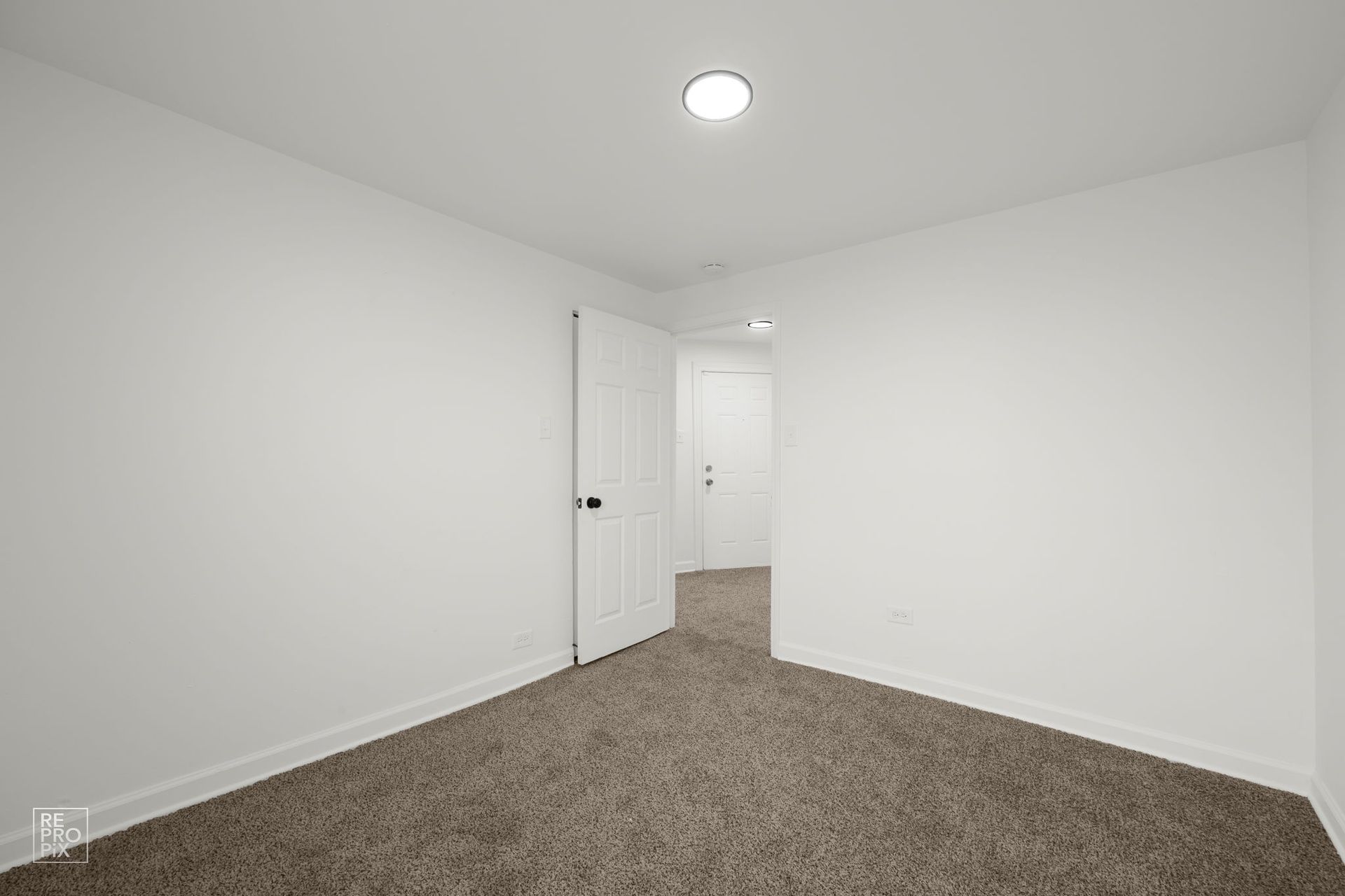 Empty room with white walls, brown carpet, and two doorways.