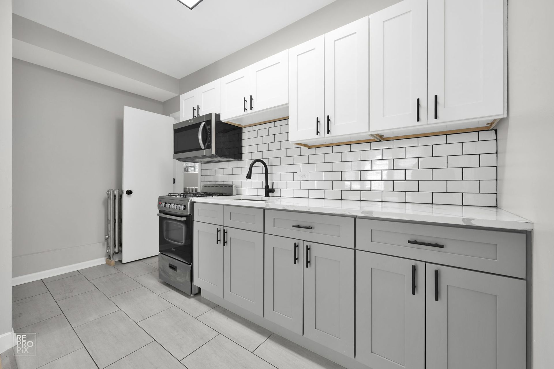 Kitchen with white and gray cabinets, subway tile backsplash, and a black microwave and stove.