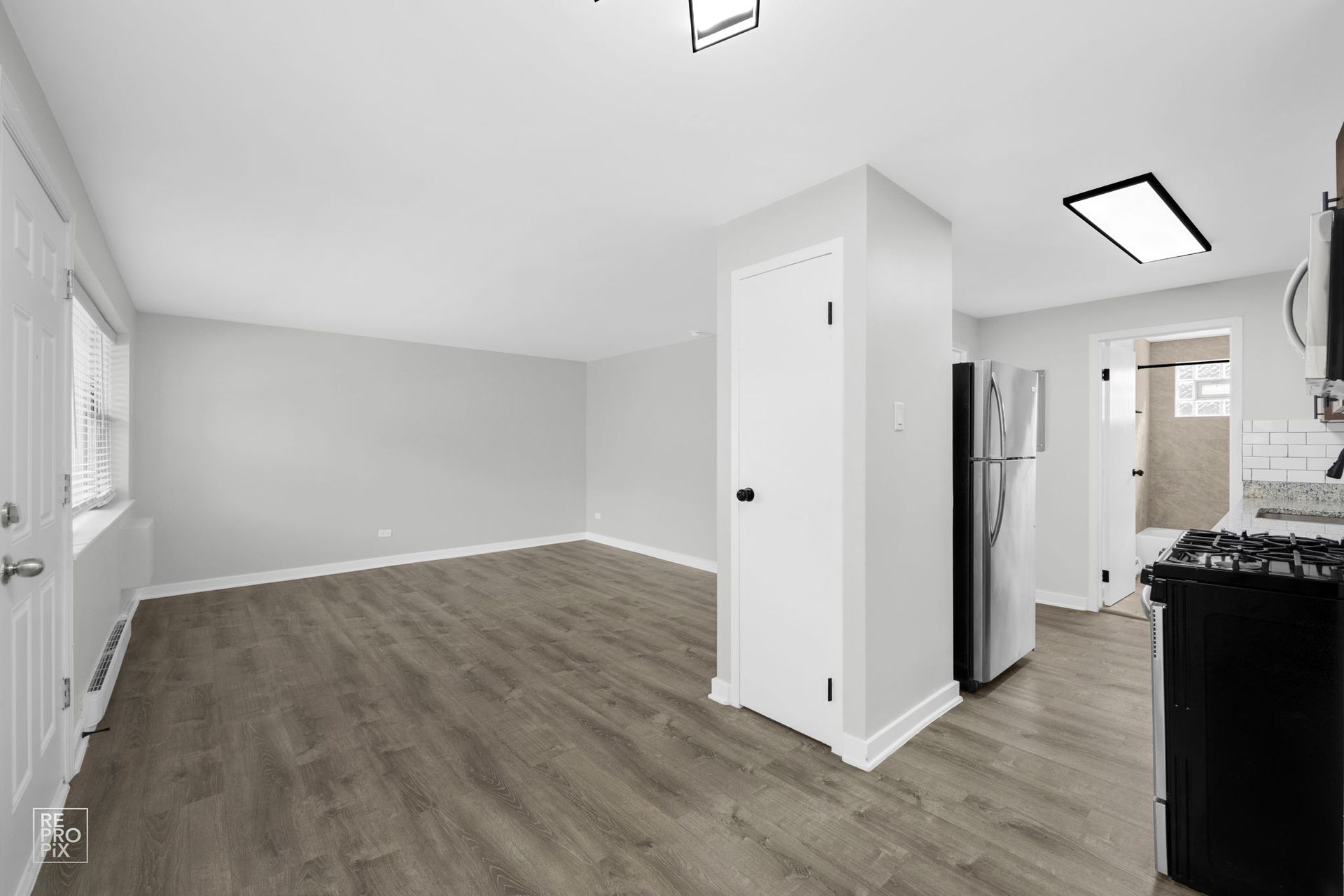 Empty apartment interior with gray walls, wood-look floor, and a stainless steel refrigerator.