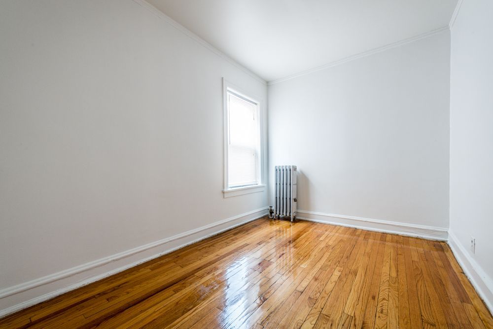Empty room with hardwood floors, white walls, window, and radiator.