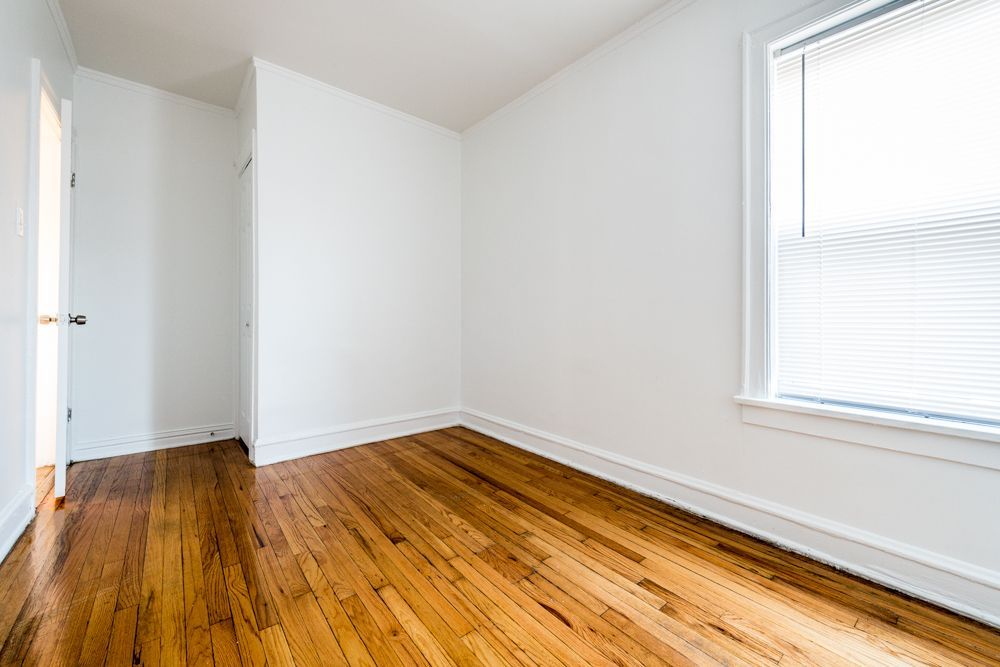 Empty room with hardwood floors, white walls, and a window with blinds.