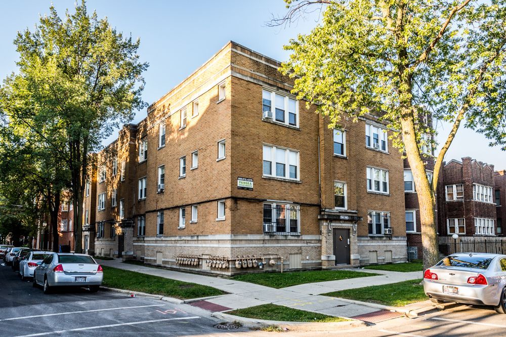 Brick apartment building with trees, cars parked on street.
