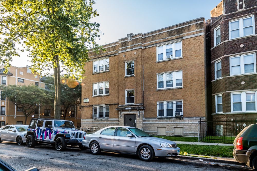Apartment building exterior with parked cars on a sunny street.